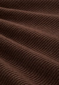 Bruine gestructureerde stof met een geribbelpatroon, met afwisselende richels en dalen, die een zachte, tactiele oppervlakte creëren.