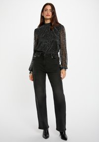 Zwarte high-waisted jeans met een rechte snit, gecombineerd met een sheer, textuur-gegeven zwarte blouse met lange mouwen, een hoge hals en subtiele glans.