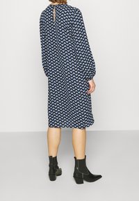 Marinblå klänning med blommönster i blått och vitt, lång ärm, lös passform och en nyckelhålsdetalj i ryggen. Svarta ankelstövlar med blockklack.