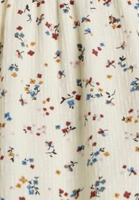 Tissu crème avec un petit imprimé floral dispersé en rouge, bleu, jaune moutarde et noir sur un fond texturé.