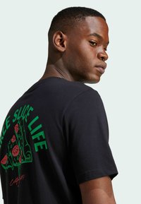 T-shirt nera con grafica colorata di una fetta di pizza con accenti rossi e verdi, con la scritta "FREE SLICE LIFE" sul retro.