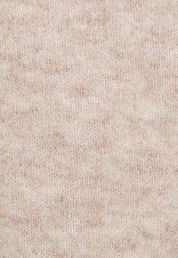 Vue en gros plan d'un tissu tricoté doux de couleur beige clair montrant la texture fine du fil et des variations subtiles de couleur.