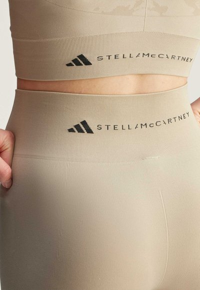 Leggings atletici beige con una texture a coste, dotati di una vita alta e di un logo nero "STELLA McCARTNEY" sulla parte superiore.