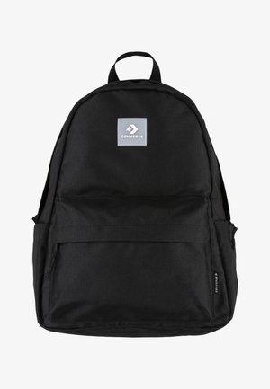 Mochila negra de lona con un compartimento principal, bolsillo delantero con cremallera y un parche de logo gris de Converse. Diseño resistente con correas ajustables.