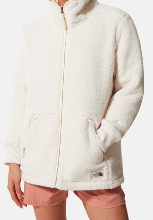Chaqueta de forro polar blanca con un alto cuello, cremallera frontal y dos bolsillos laterales. Presenta puños acanalados y un pequeño logo en el dobladillo.