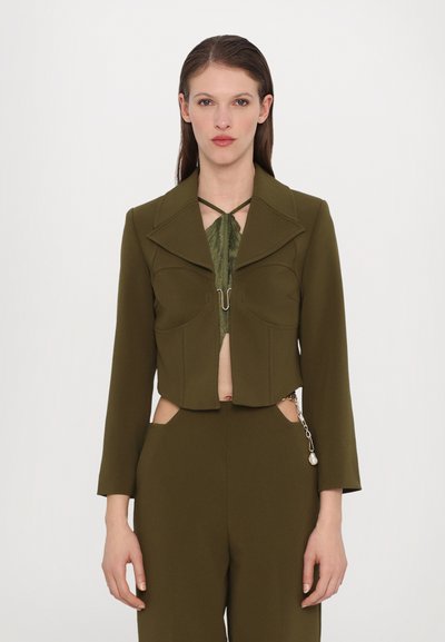 Veste courte vert olive avec un large col, deux poches au devant et une fermeture à crochet. Le matériau a une texture lisse et une coupe structurée.