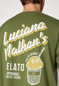 Olive green t-shirt featuring bold, white and yellow text and a graphic of an ice cream cone with a spoon, labeled "ELATO."