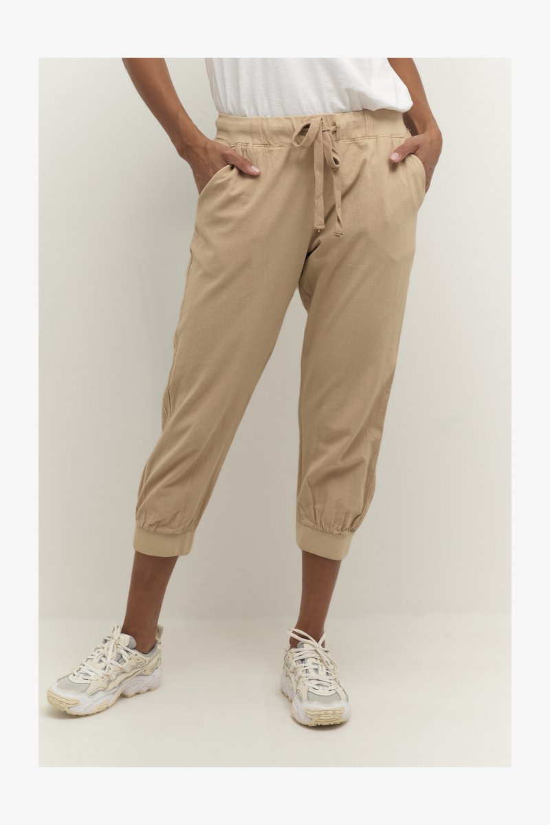 Beige cropped trousers with elastic cuffs and a drawstring waist. Made of soft fabric, featuring side pockets for utility.