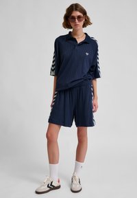 Navyrandig polo och shorts-set med chevronmönstrade sidodekaler, bärs med vita strumpor och sneakers. Avslappnad sportklädesdesign.