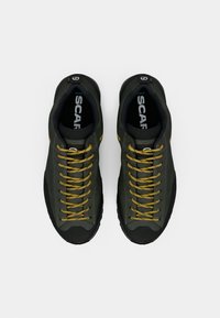 Dark green sneakers with yellow laces, a textured upper, rubber soles, and a rounded toe design. Logo visible on the inner side.