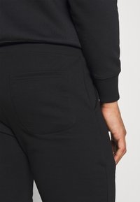 Black sweatpants featuring a slim fit, a back pocket, and ribbed cuffs. Material appears soft with a smooth texture.