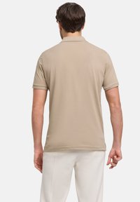 Beige poloshirt met een zachte textuur en korte mouwen, voorzien van een puntige kraag en een rechte zoom, gecombineerd met lichtgekleurde broeken.