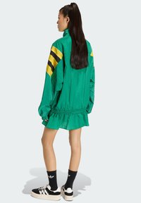 Zelená vetrovka so žltými pruhmi, volánovým lemom a pružnými manžetami. Kombinovaná s čiernymi teniskami a čiernymi ponožkami s logom.