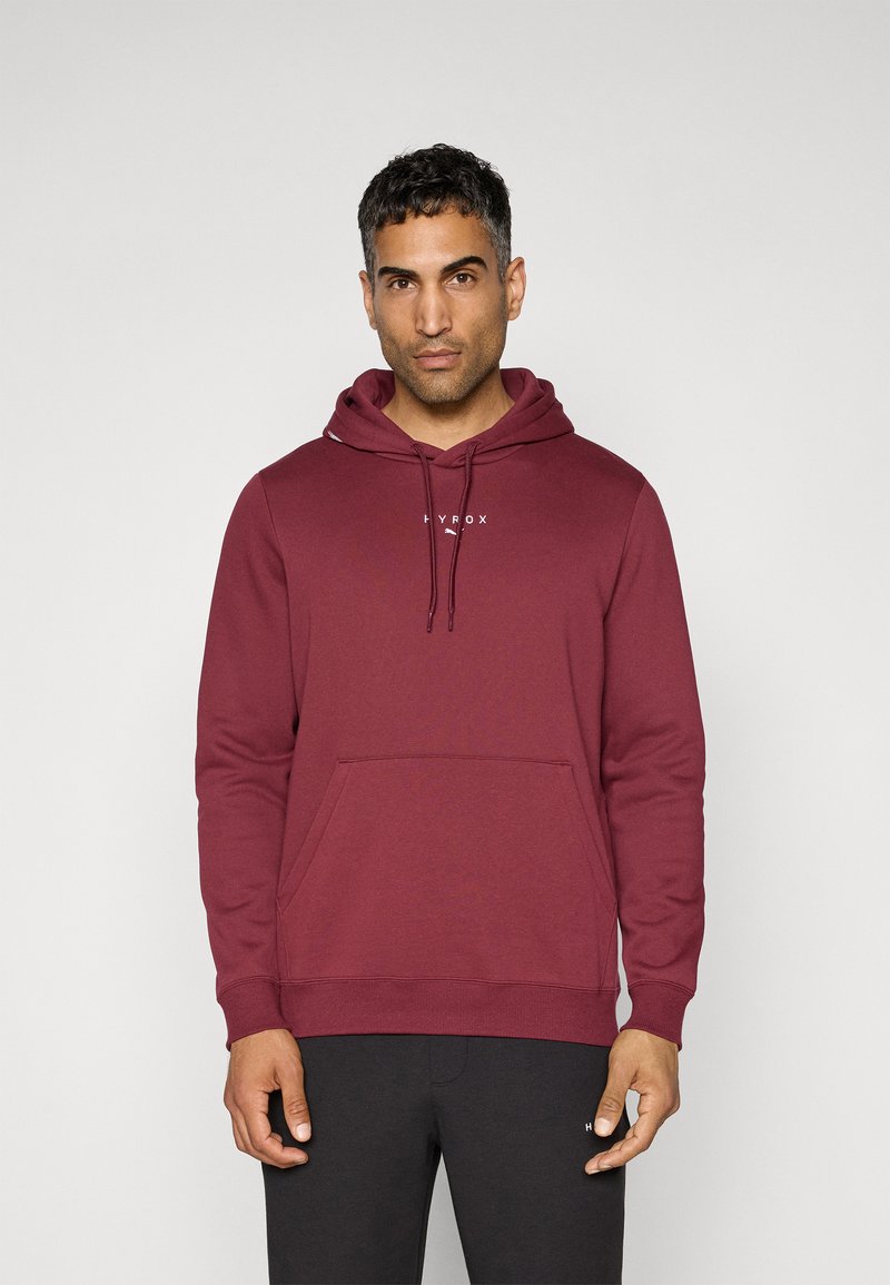 Maroonsweater med en frontlomme, snoretræk i huen og hvidt logo på brystet. Stoffet er blødt med en glat overflade.
