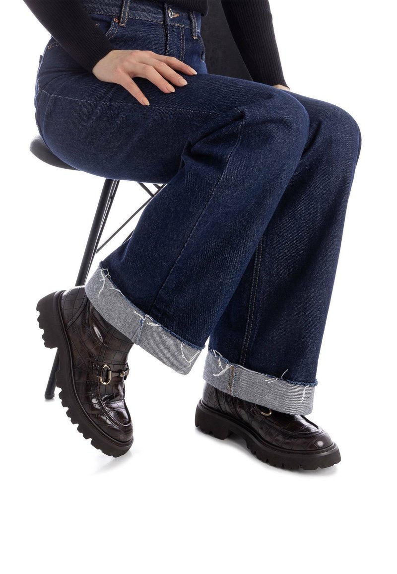 Ciemnoniebieskie jeansy o szerokich nogawkach z postrzępionym jasnoniebieskim mankietem, w połączeniu z błyszczącymi czarnymi butami na obcasie z teksturowanym wykończeniem i detalem zapięcia.