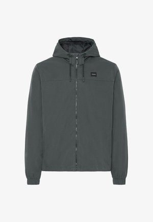 Szürke kapucnis dzseki, elöl cipzárral, rugalmas mandzsettákkal és oldalsó zsebekkel. Sima textúra és egyszerű, minimalista dizájn. Márkacímke a mellkasán.