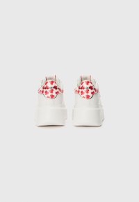 Baskets blanches avec une semelle épaisse, présentant un motif de feuilles rouges sur le talon, et un logo "Karl Lagerfeld" en argent. Texture en cuir lisse.