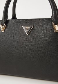Sac à main noir texturé avec une plaque logo en forme de triangle en ton or, des poignées doubles et des accents en métal.