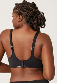 Sujetador inalámbrico negro con tirantes ajustables, cierre de enganche y tejido suave. Diseño sencillo sin patrones ni adornos visibles.