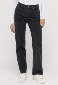 Schwarze Cordhose mit geradem Schnitt; verfügt über Fronttaschen und einen Metallknopf am Bund; kombiniert mit weißen Sneakers.