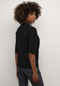 Suéter de punto negro de manga corta con un escote redondo y un ajuste ligeramente holgado. La tela tiene un brillo sutil, combinado con jeans oscuros.