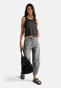 Top crop nero, jeans grigi larghi, borsa tote intrecciata nera, sandali neri con accenti metallici, collana in catena argentata, capelli lisci.