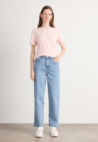 T-shirt en coton rose clair à manches courtes avec un petit logo, associé à un jean droit taille haute bleu clair et des chaussures blanches.