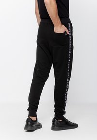 Czarne dresy o dopasowanym kroju, z elastycznym paskiem i kieszeniami bocznymi, zdobione wzorzystymi białymi akcentami po bokach. Wykonane z miękkiego, elastycznego materiału.