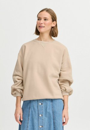 Lichtbeige sweatshirt met een ronde halslijn en verlaagde schouders, gecombineerd met een blauwe denim rok met knoopdetails aan de voorkant.