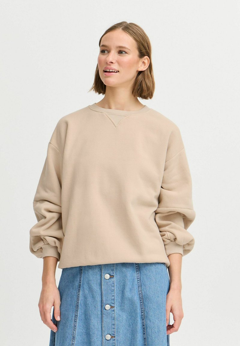 Sweatshirt beige clair avec un col rond et des épaules tombantes, associé à une jupe en denim bleue avec des détails de boutons à l'avant.