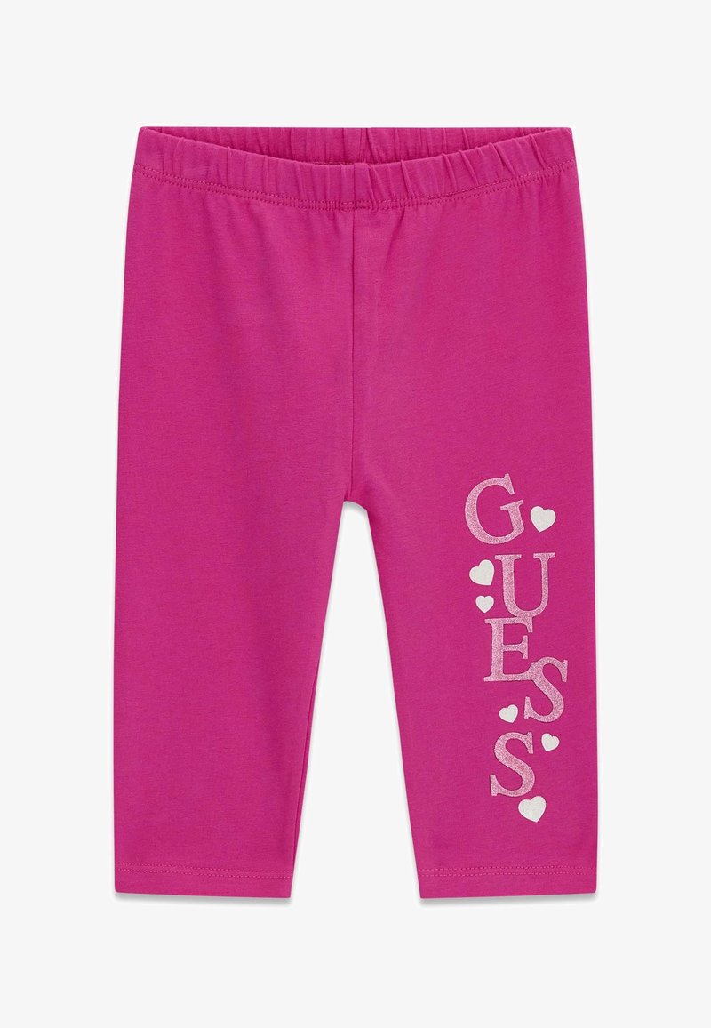 Leggings pour enfants rose vif avec taille élastique et logo vertical « GUESS » décoré de petits cœurs sur la jambe droite.