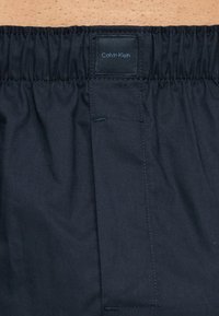 Κοντινή λήψη μαύρου εσώρουχου boxer Calvin Klein με ελαστική μέση πάνω σε γυμνό δέρμα.