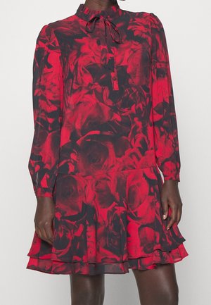 Langärmeliges rotes und schwarzes Blumenmusterkleid mit gerafftem Saum und Halsband, getragen von einer Person mit dunklem Hautton vor schlichtem Hintergrund.