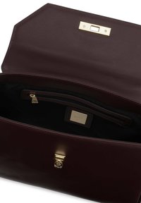 Burgundowa skórzana torebka o strukturalnym designie, złotym okuciu i wewnętrznej kieszeni na zamek. Gładka tekstura z kontrastującymi detalami ściegów.