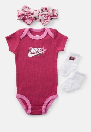 Rosa bomullsbody med korte ermer, kontrasterende rosa kant, og Nike-logo prydet med blomstrete detaljer. Inkluderer hvite sokker med logo og blomsterhodebånd.