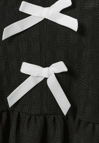 Tessuto nero testurizzato con fiocchi in raso bianchi e un dettaglio di ruffle arricciato, che mette in risalto intricati motivi e colori contrastanti.
