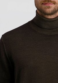 Dunkelbrauner Rollkragenpullover aus Rippstrick, mit hohem Kragen und figurbetontem Design, geeignet für kühleres Wetter.