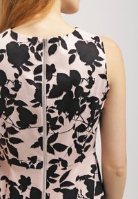 Robe à motifs floraux avec un fond rose clair et des feuilles noires, un col rond et une fermeture éclair au dos.