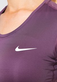 Camiseta sin mangas deportiva de color púrpura con escote redondo, que presenta un logo de Nike blanco en el lado izquierdo y un diseño liso y ajustado.