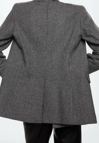 Veste à carreaux gris avec une coupe ajustée, dotée d'un large revers, d'une fente arrière et de deux poches latérales, fabriquée en tissu texturé.