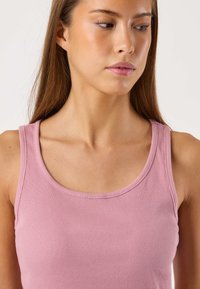 Lichtroze geribde tanktop met een ronde halslijn. Zachte textuur, aansluitende pasvorm, zonder extra patronen of hardware-details.