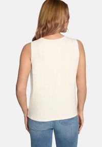 Blouse crème sans manches avec un col rond, une texture douce et une coupe décontractée, associée à un jean en denim bleu clair.