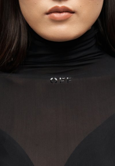 Κοντινό πλάνο του κάτω μέρους του προσώπου και του λαιμού ενός ατόμου που φοράει μαύρο ζιβάγκο με την λέξη "OFF" τυπωμένη κοντά στον γιακά.