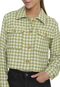 Veste courte à motif pied-de-poule vert et blanc, avec un col, deux poches poitrine et des boutons beige. Tissu tissé texturé.