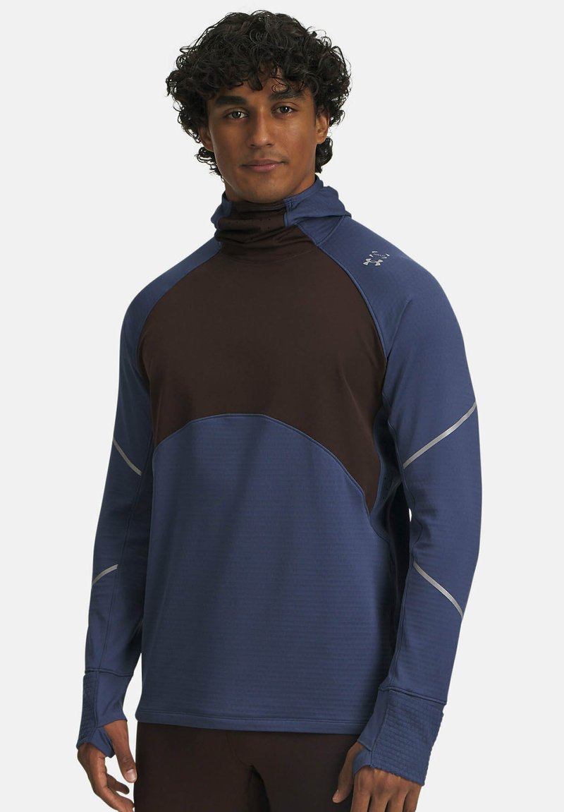Maglia sportiva a collo alto in blu e marrone. Presenta un colletto alto, tessuto testurizzato, dettagli riflettenti e maniche lunghe con aperture per il pollice.