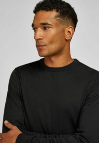 Zwarte ronde hals trui van een gladde stof, met een geribbelde halslijn en lange mouwen. De pasvorm is comfortabel en tailored.