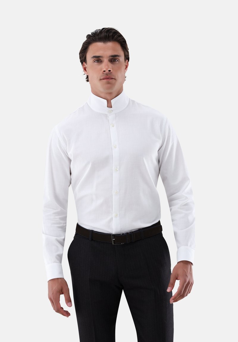 Camicia bianca a maniche lunghe con colletto alla coreana, caratterizzata da una chiusura con bottoni, abbinata a pantaloni scuri a righe sottili e una cintura marrone.