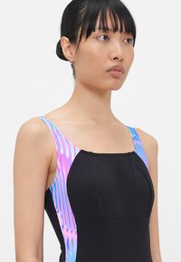 Maillot de bain noir au design ajusté, présentant des accents colorés et ondulés en violet et bleu le long des bretelles et des côtés. Texture lisse.