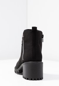 Stivale alla caviglia nero con tomaia texture, zip laterale e tacco spesso a coste. Dotato di un tassello sul retro per indossarlo facilmente.