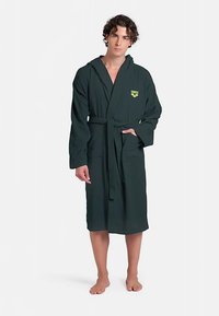 Dunkelgrüner Bademantel mit strukturierter Stoffqualität, Kapuze und gebundenem Taillenband. Verfügt über ein kleines gelbes Logo auf der Brust und zwei Seitentaschen.
